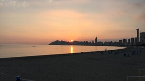 Une plage avec une vue sur les gratte-ciel d’une ville en arrière-plan, un ciel dégagé et une mer calme.