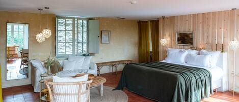 A room with a bed, a sofa, a wicker chair, a small table, and a window.