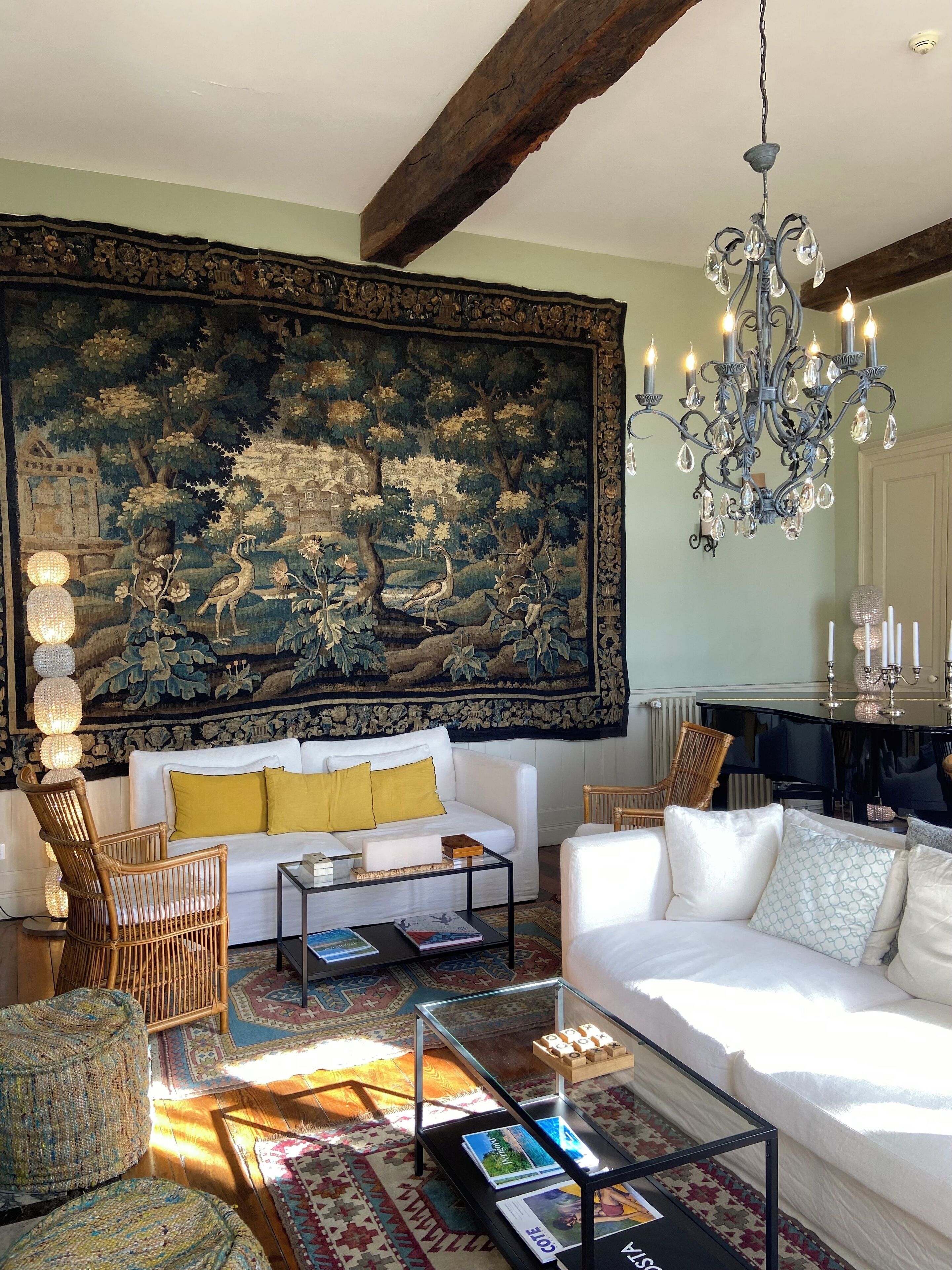 Ein Wohnzimmer mit einem großen Wandteppich, einem weißen Sofa, einem Glastisch und einer Chandelier.
