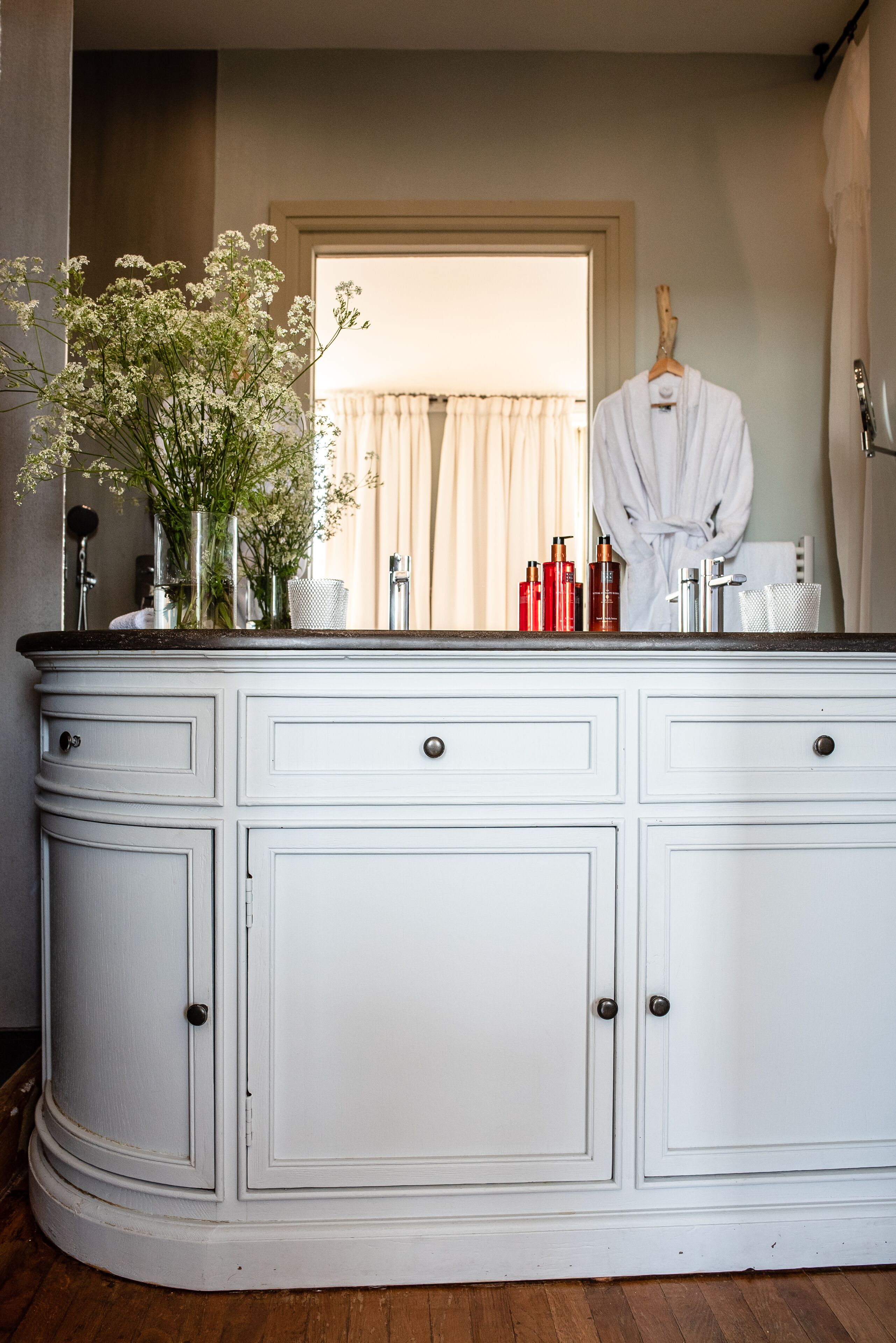 Un mobile bagno bianco con uno specchio, un vaso con fiori e un accappatoio appeso.