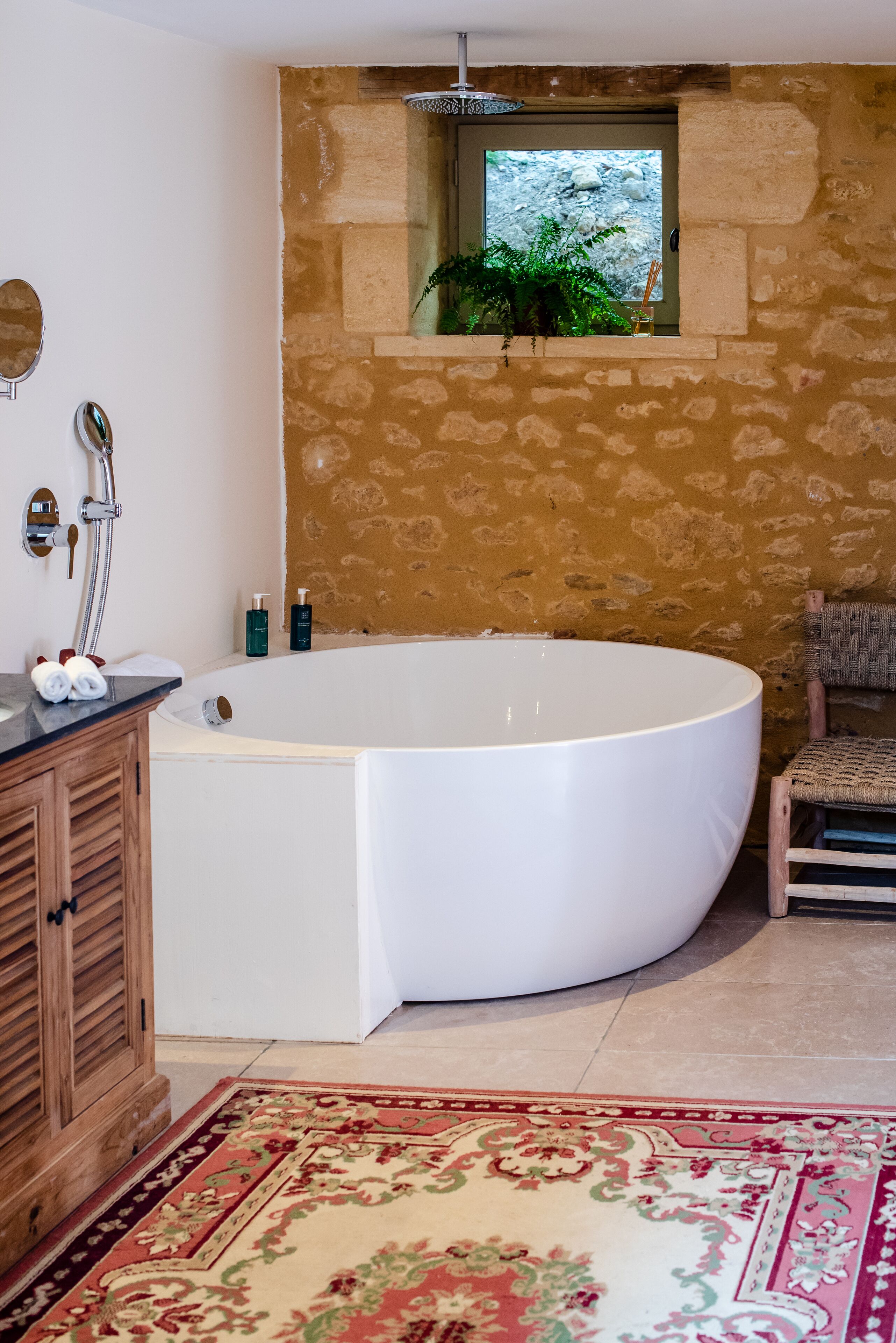 Ein Badezimmer mit einer großen Badewanne, einem Holzkabinett, einem Spiegel und einem Fenster mit Blick auf eine felsige Landschaft.