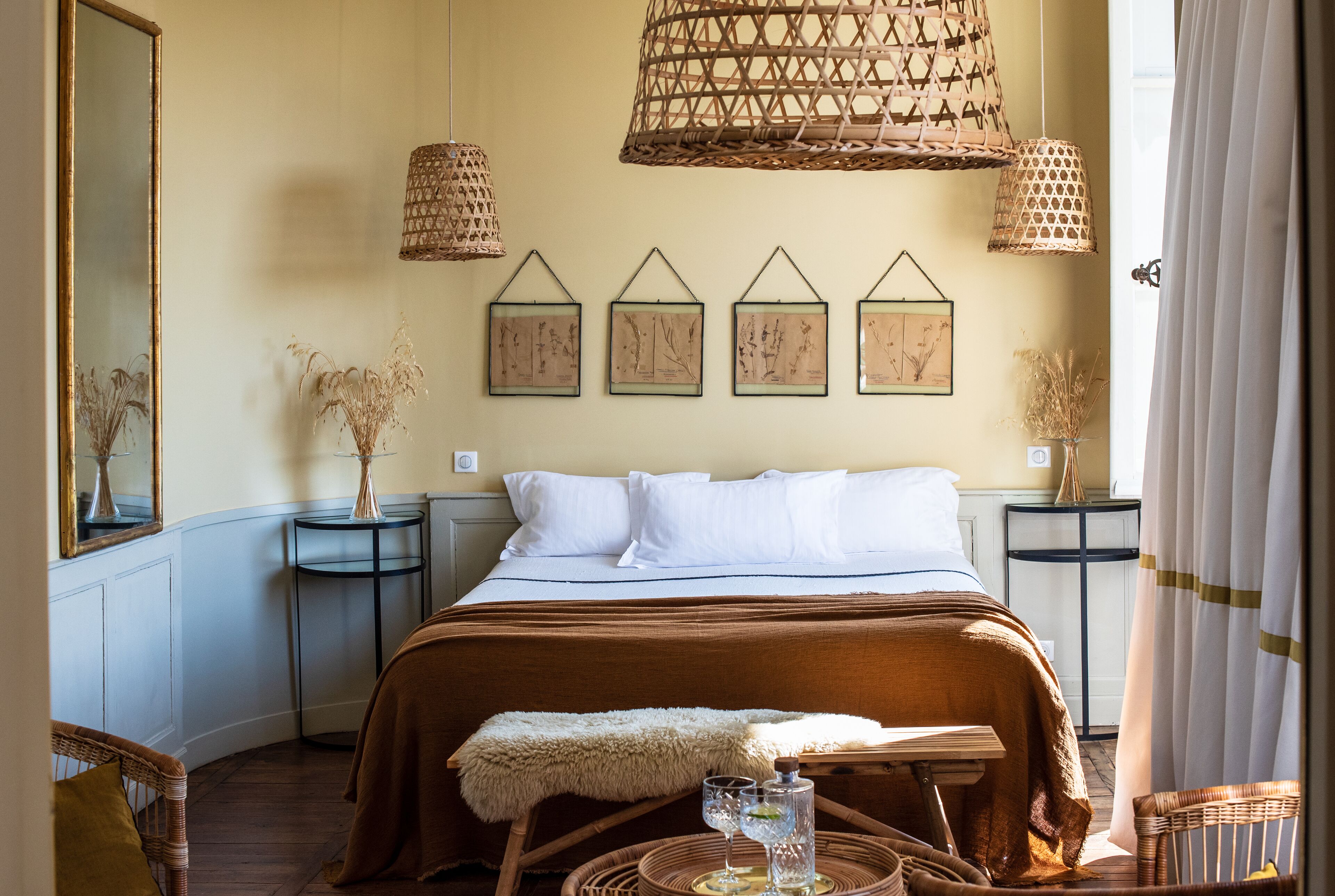 A bedroom with a large bed, two bedside tables, a mirror, and a hanging light fixture.