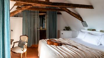 Quarto com teto de madeira, uma cama com um violão, uma cadeira e uma janela com cortinas.