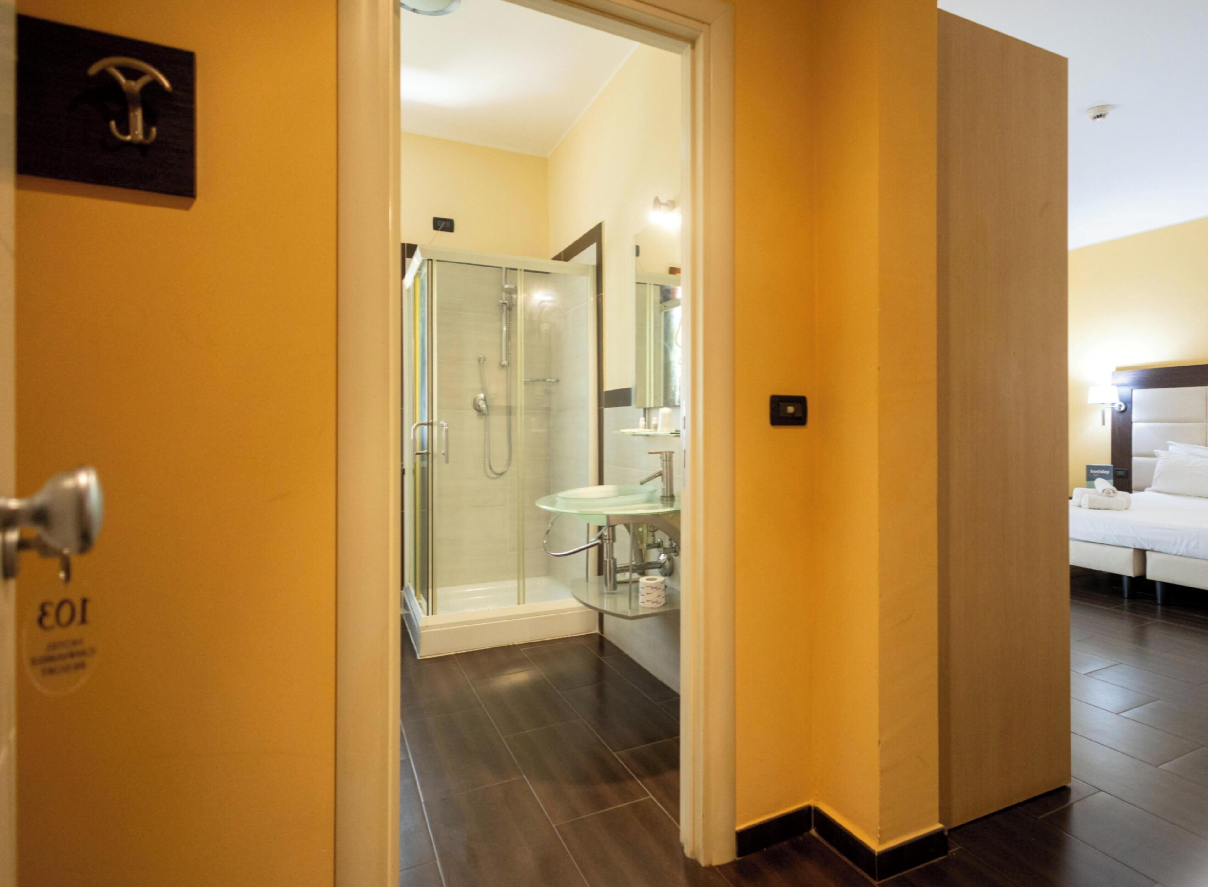 A hotel room with a bed, a bathroom with a glass shower, and a visible door handle.