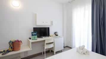 Habitació d'hotel amb llit, escriptori amb ordinador, cadira, taula petita amb cistella i finestra amb cortines.