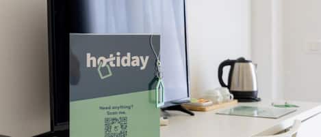 A hotel desk with a monitor displaying a 'holiday' sign and a QR code for 24/7 AI chat on WhatsApp.