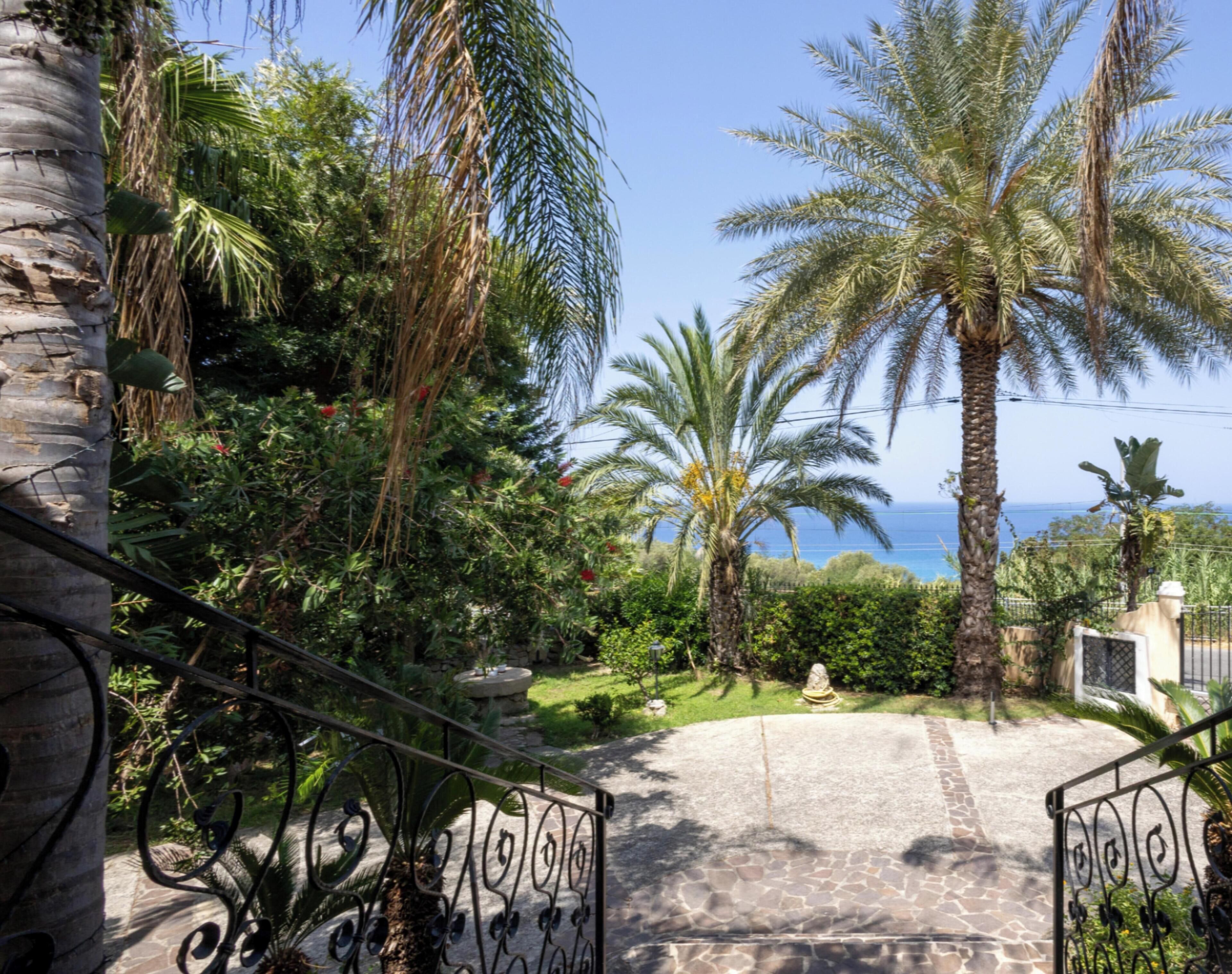 A paved pathway leading to a gated entrance with a view of the sea.