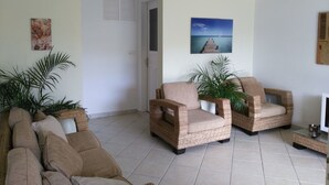 A living room with two wicker armchairs, a beige sofa, and a television on a stand.