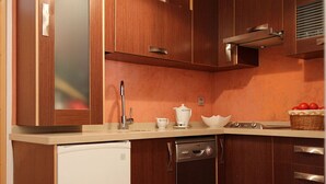 Una cocina compacta con armarios de madera, lavavajillas y una pequeña encimera con fregadero y hervidor.