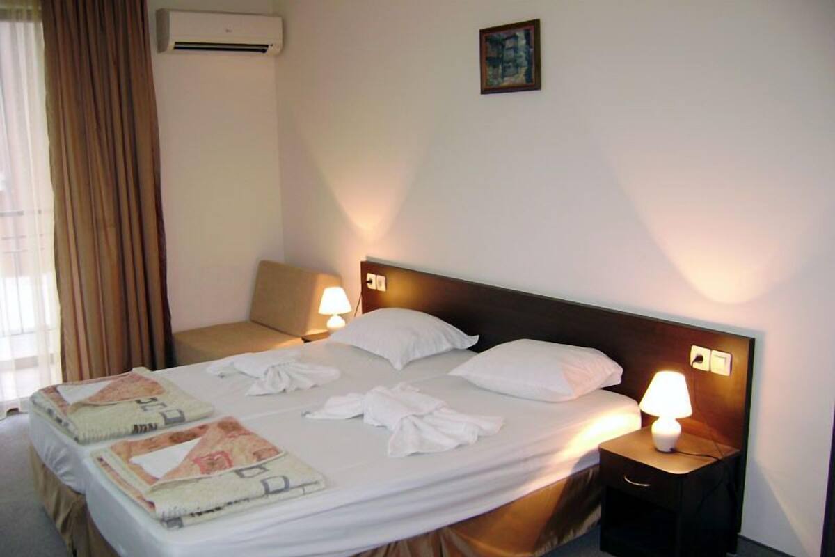 Une chambre d’hôtel avec un lit, deux lampes de chevet, une table de chevet, une fenêtre avec des rideaux et un climatiseur fixé au mur.