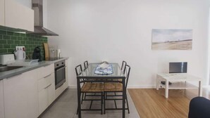 Una cocina moderna con armarios blancos, un salpicadero verde y una zona de comedor con mesa y sillas de vidrio.