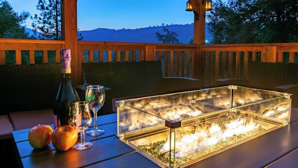 A glass display case with a fire feature, a bottle, wine glasses, and apples on a wooden table.
