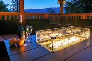 A glass display case with a fire feature, a bottle, wine glasses, and apples on a wooden table.