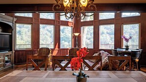 A room with large windows, a chandelier, wooden furniture, and a fireplace.