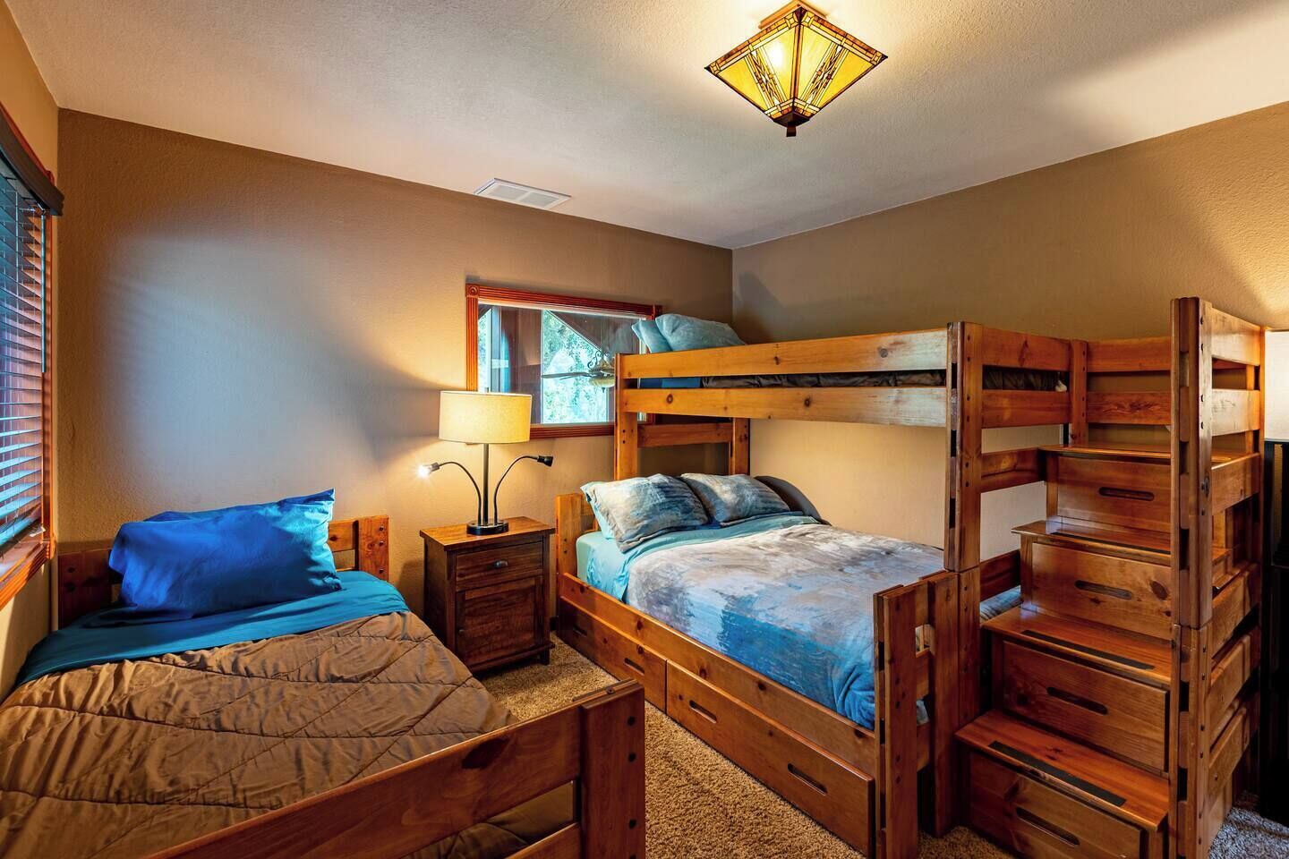 A room with bunk beds, a bedside table with a lamp, a mirror, and a window with blinds.