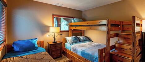 A room with bunk beds, a bedside table with a lamp, a mirror, and a window with blinds.