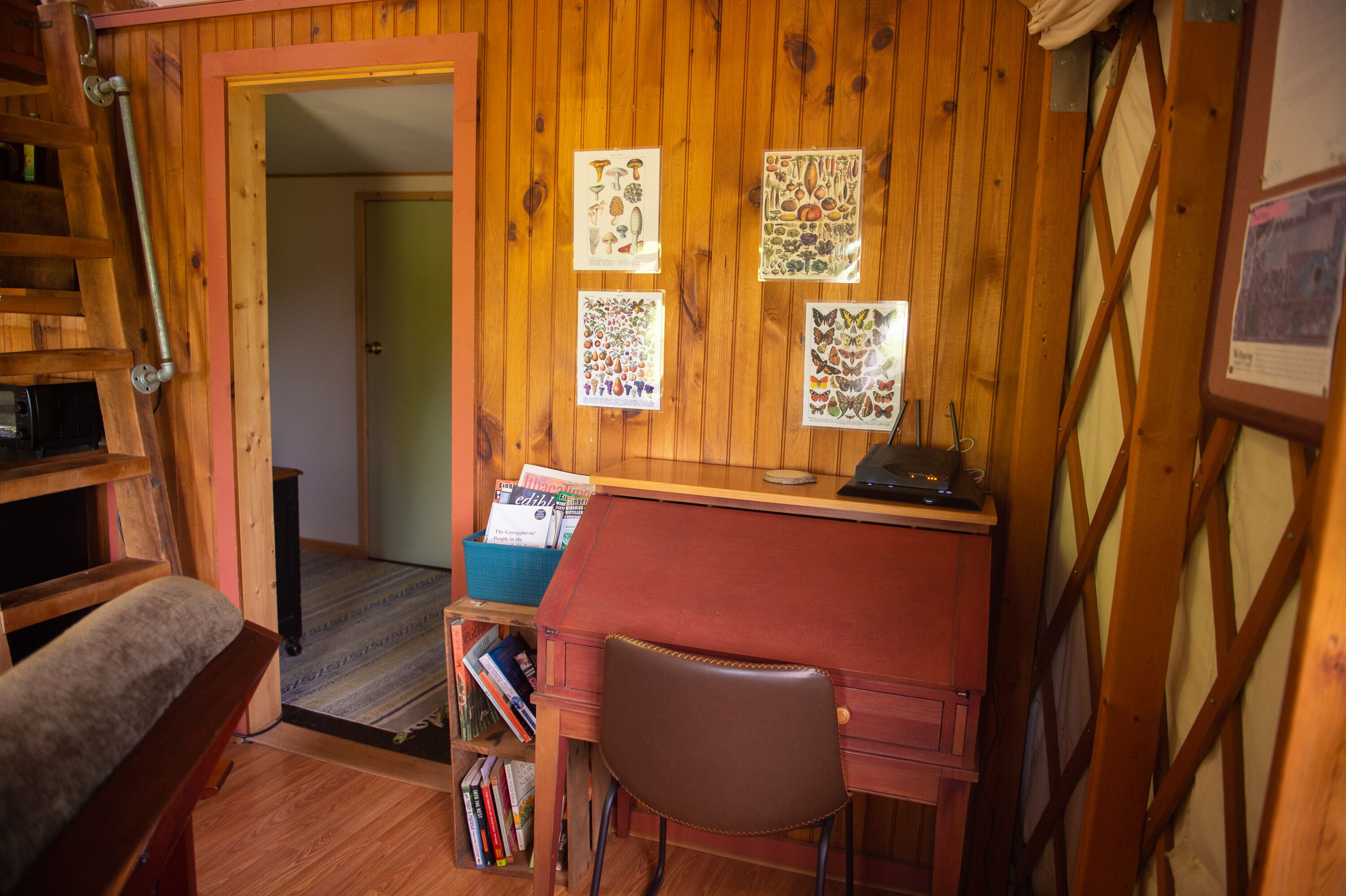 Una habitación de madera con un escritorio, una silla y una escalera. Hay carteles en la pared y una estantería llena de libros.