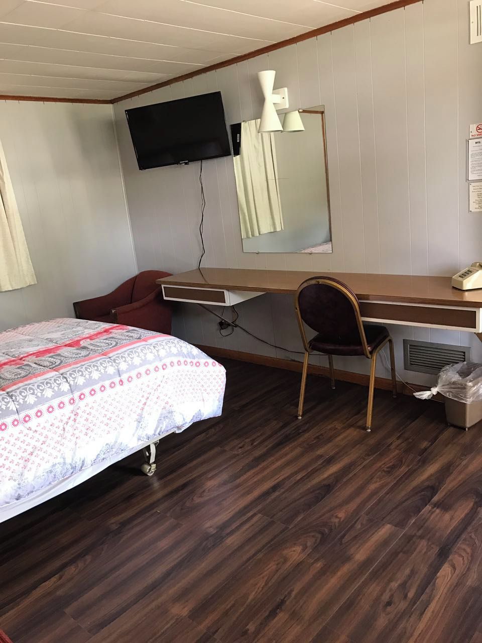 A bedroom with a bed, a desk, a chair, a television, and a mirror.
