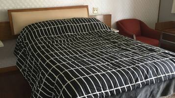 A neatly made bed with a black and white checkered bedspread, a wooden headboard, and a quilted mattress. There is a red chair and a wooden nightstand with a lamp.