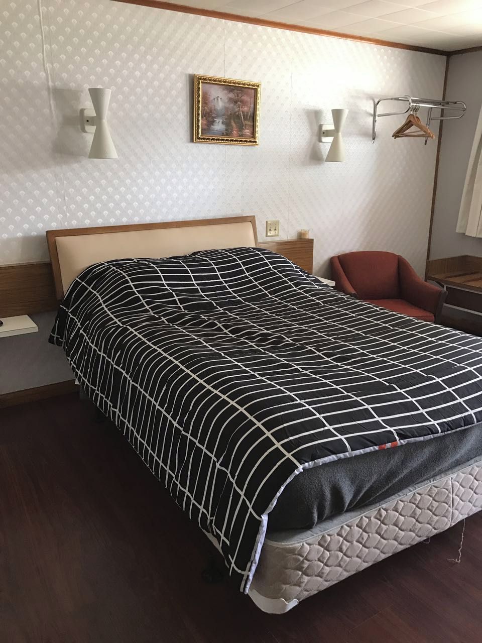 A hotel room with a bed, a chair, a bedside table, and a wall-mounted lamp.