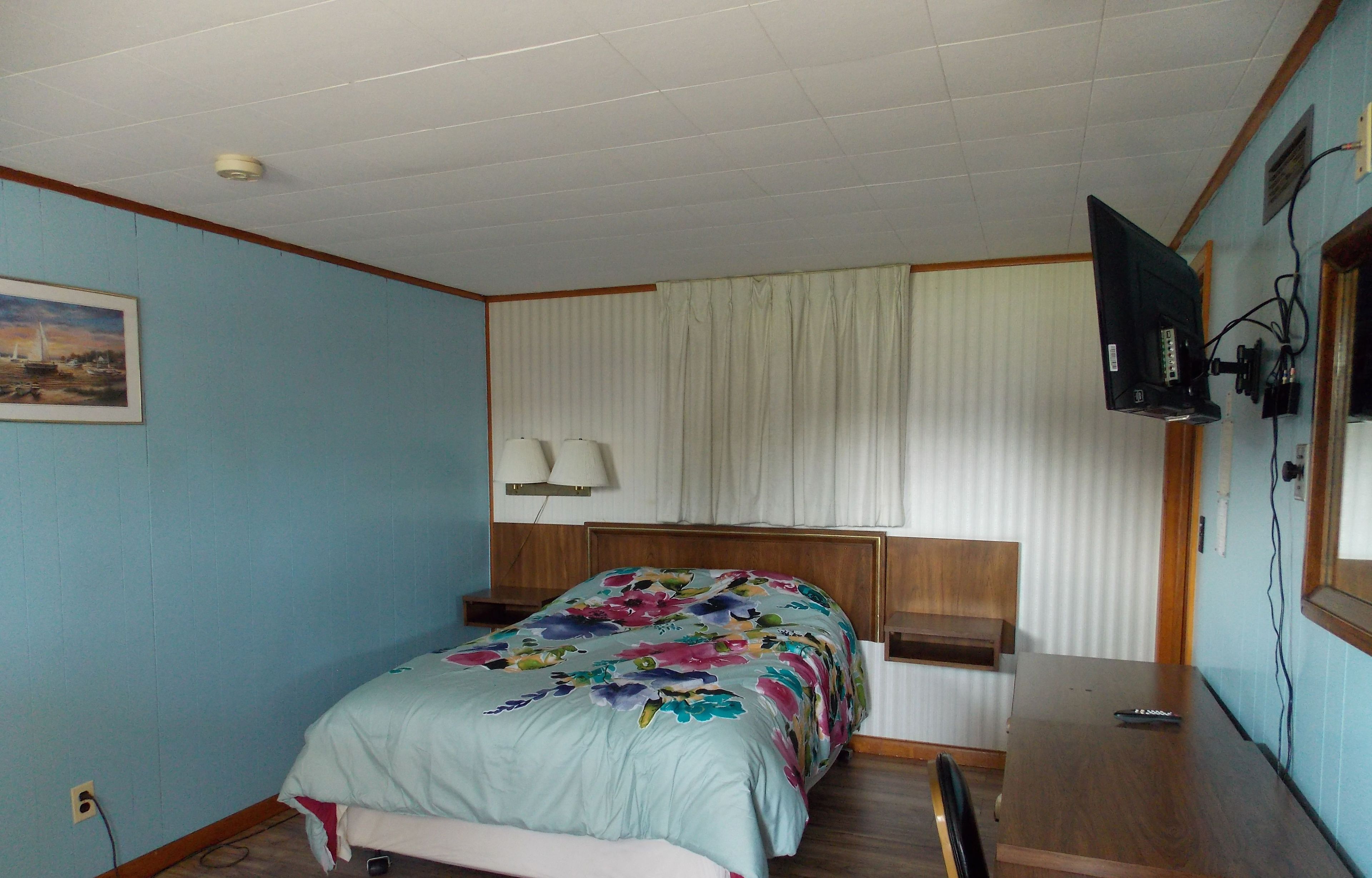 Un dormitorio con cama, escritorio, televisor y ventana con cortinas.