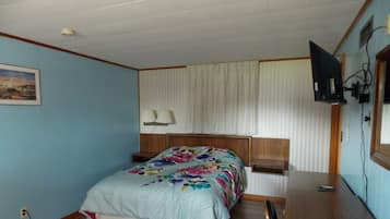 Un dormitorio con cama, escritorio, televisor y ventana con cortinas.
