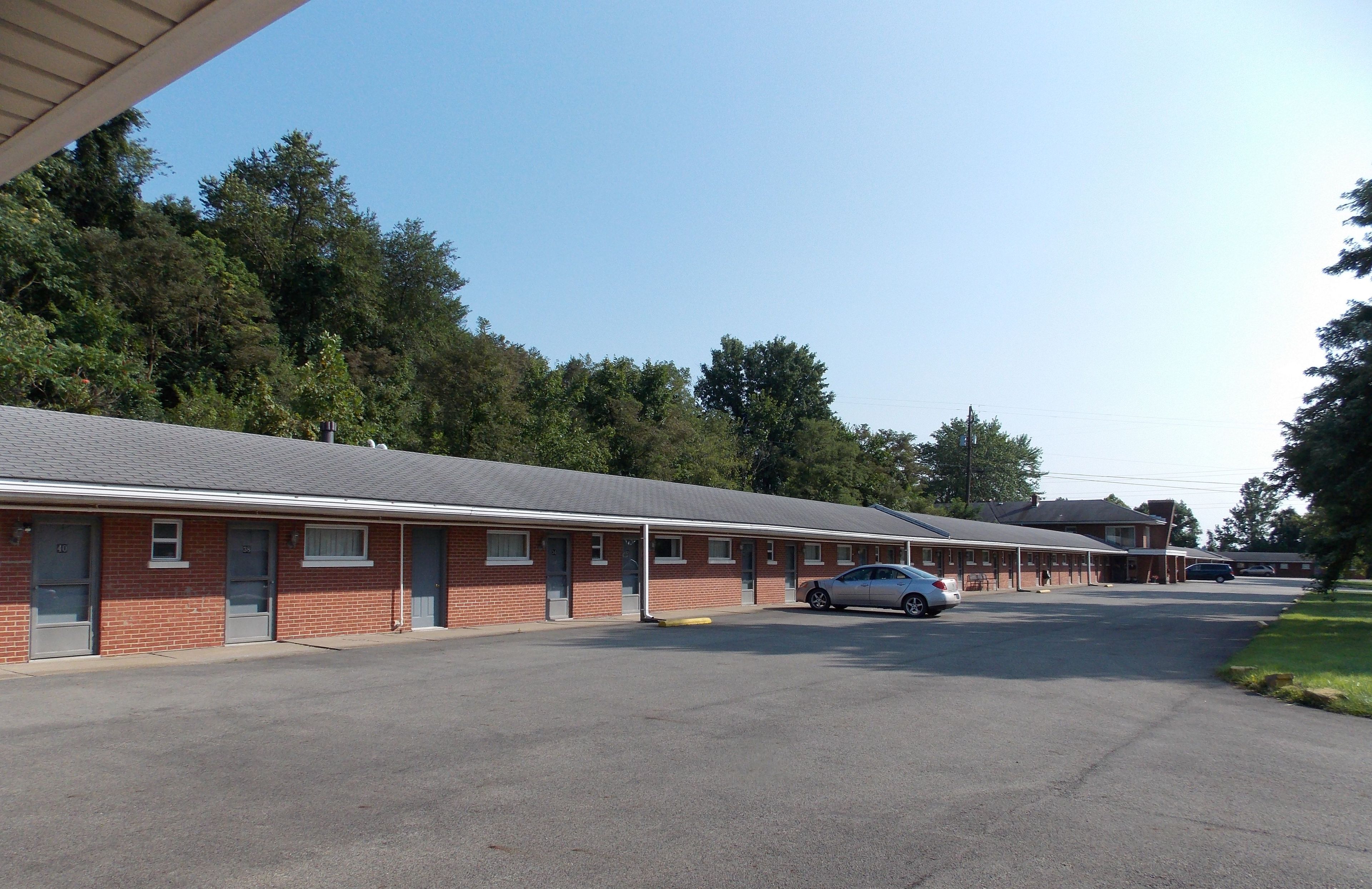 A row of single-story motel buildings with a parking lot in front.