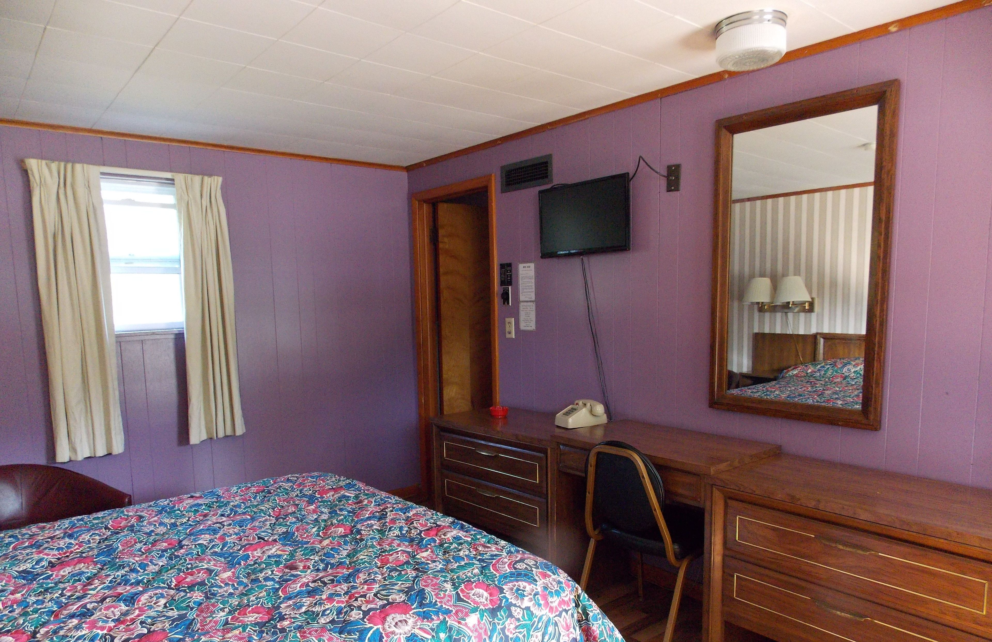 A room with a bed, a desk, a chair, a dresser, a television, and a mirror.