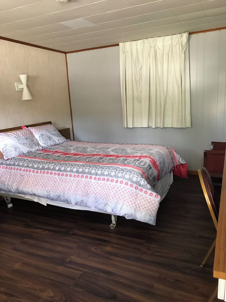 A bedroom with a bed, a nightstand, a lamp, and a window with curtains.