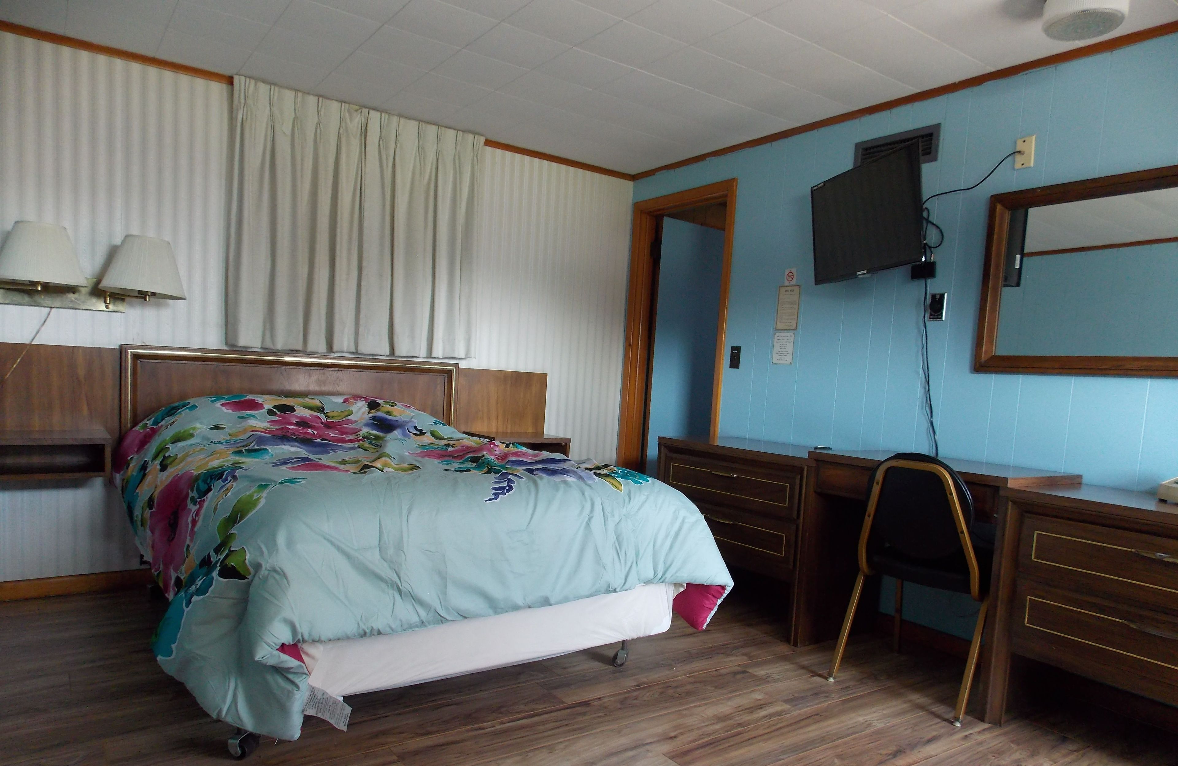 A bedroom with a bed, a desk, a chair, a television, and a mirror.