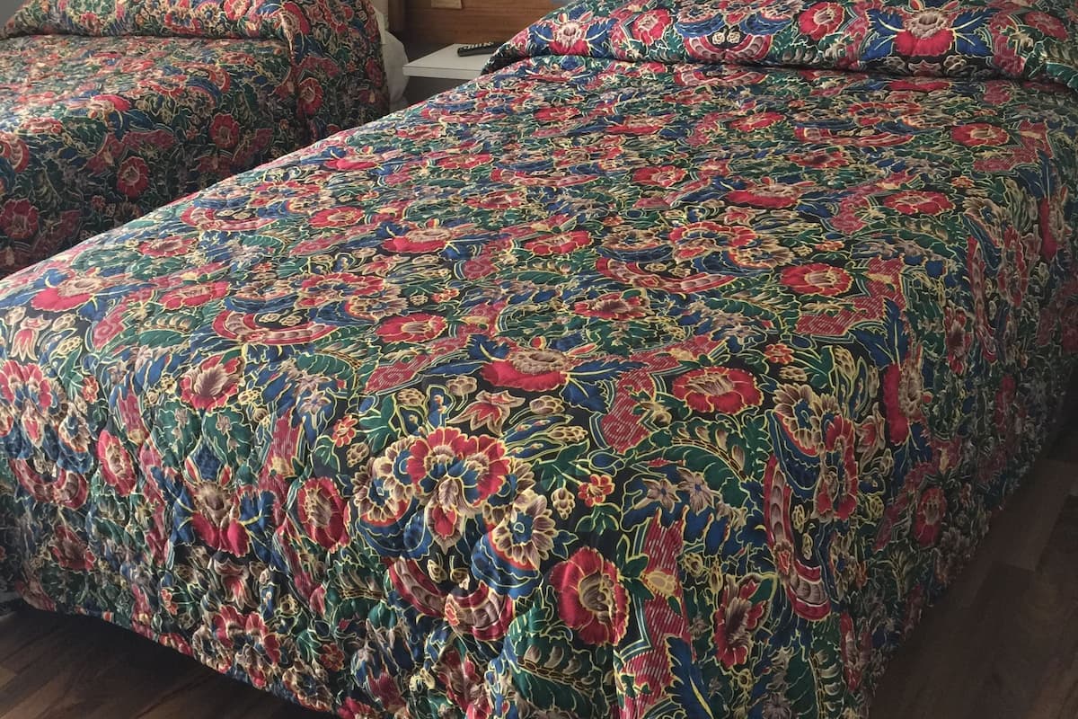 A hotel room with two beds, each with floral-patterned bedding, a wooden headboard, and a small bedside table.