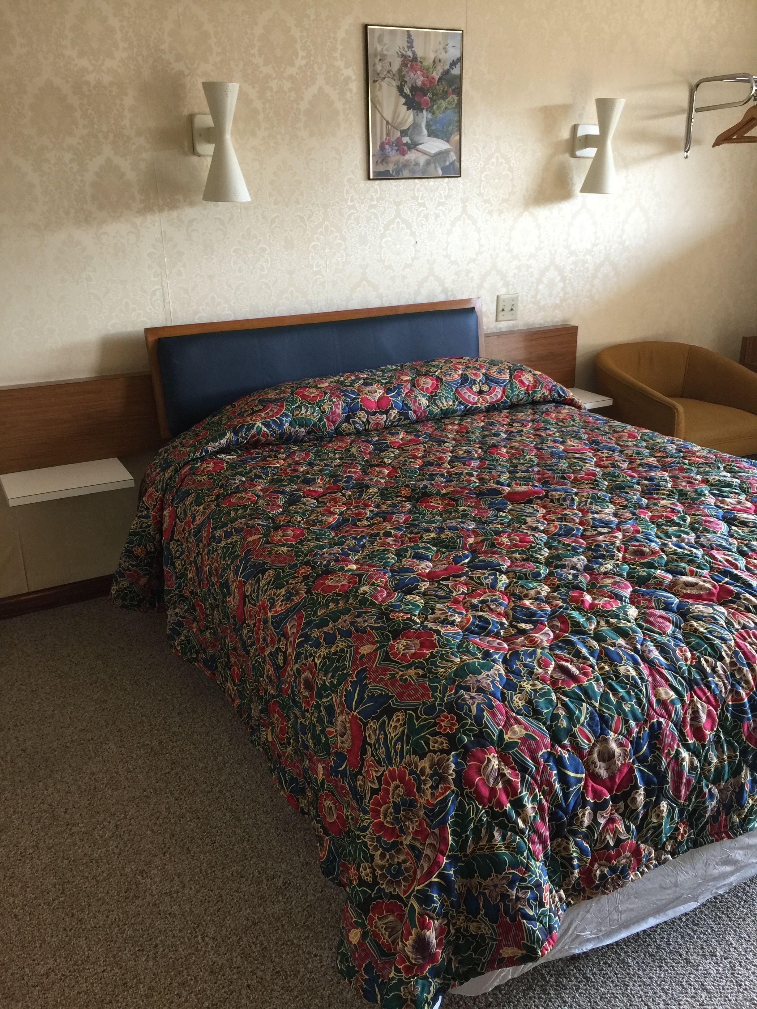 Een hotelkamer met een bed, nachtkastje, stoel en wandlampen.
