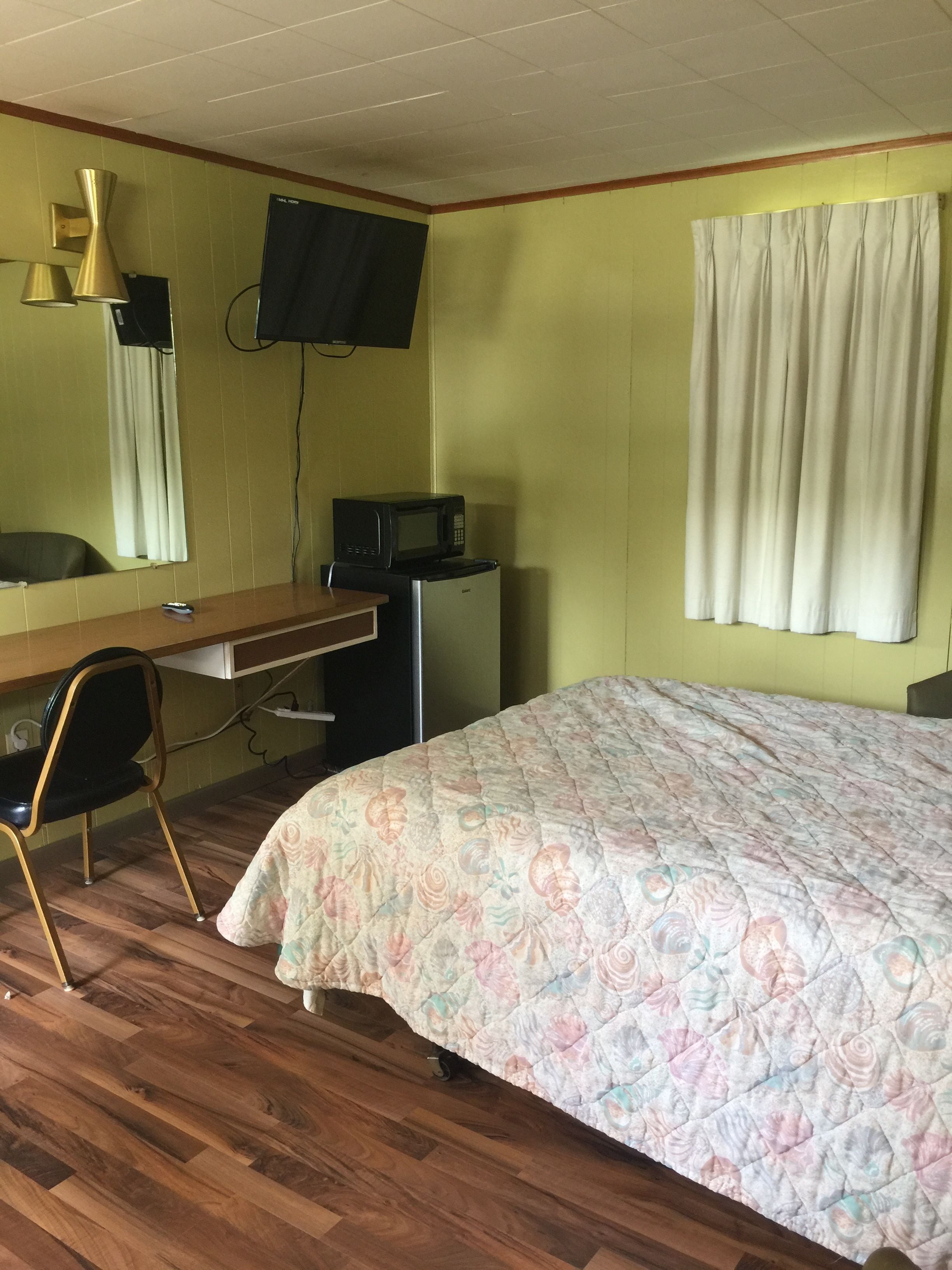 A room with a bed, a desk, a chair, a television mounted on the wall, and a microwave on a small table.
