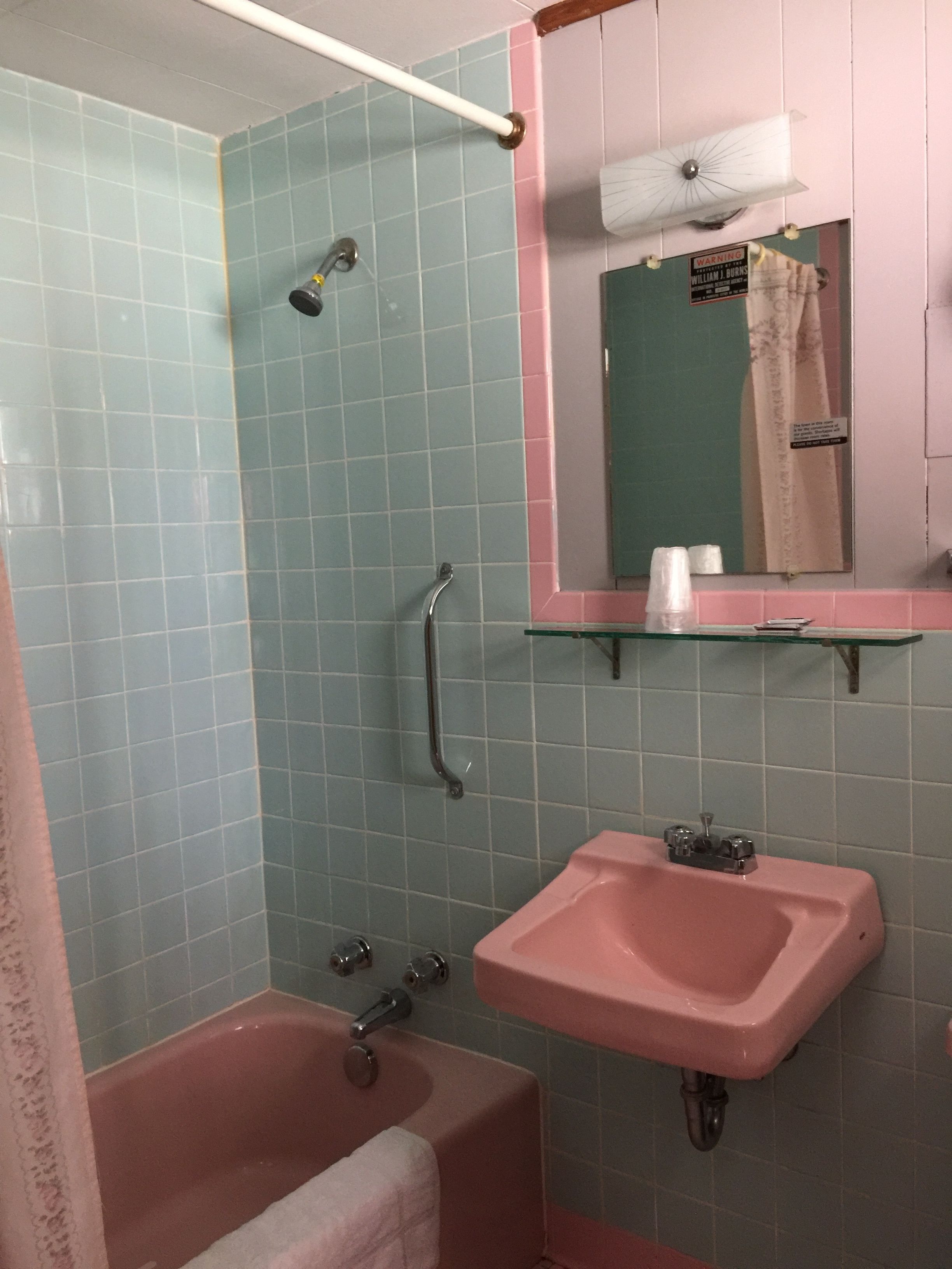 A bathroom with a pink sink, a shower with a glass door, and a mirror above the sink.