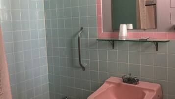 A bathroom with a pink sink, a shower with a glass door, and a mirror above the sink.