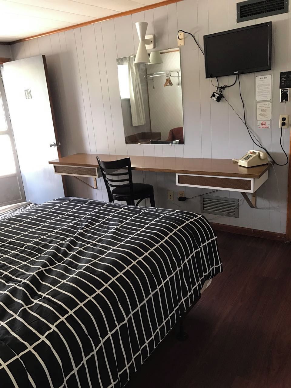 A hotel room with a bed, a desk, a chair, a television, and a mirror.