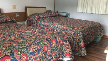 Un dormitorio con dos camas, suelo de madera, pared blanca, un cuadro enmarcado y una ventana con cortinas.