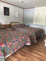 Un dormitorio con dos camas, suelo de madera, pared blanca, un cuadro enmarcado y una ventana con cortinas.