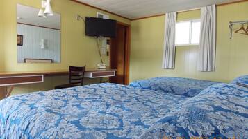 Una habitación con cama, escritorio, silla, teléfono, televisor y ventana con cortinas.