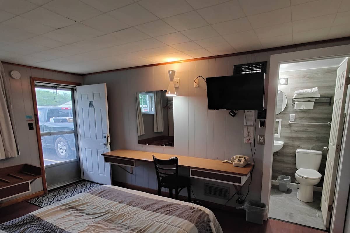A hotel room with a bed, a desk, a chair, a TV, and a bathroom.