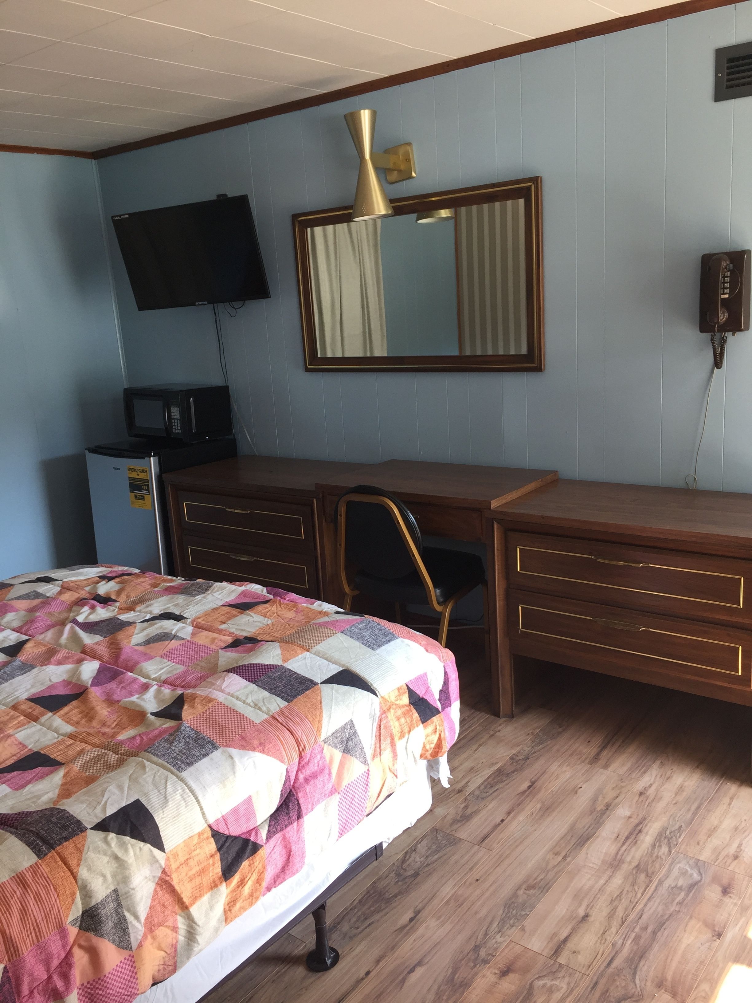 A bedroom with a bed, a desk, a chair, a television, a mirror, and a telephone.