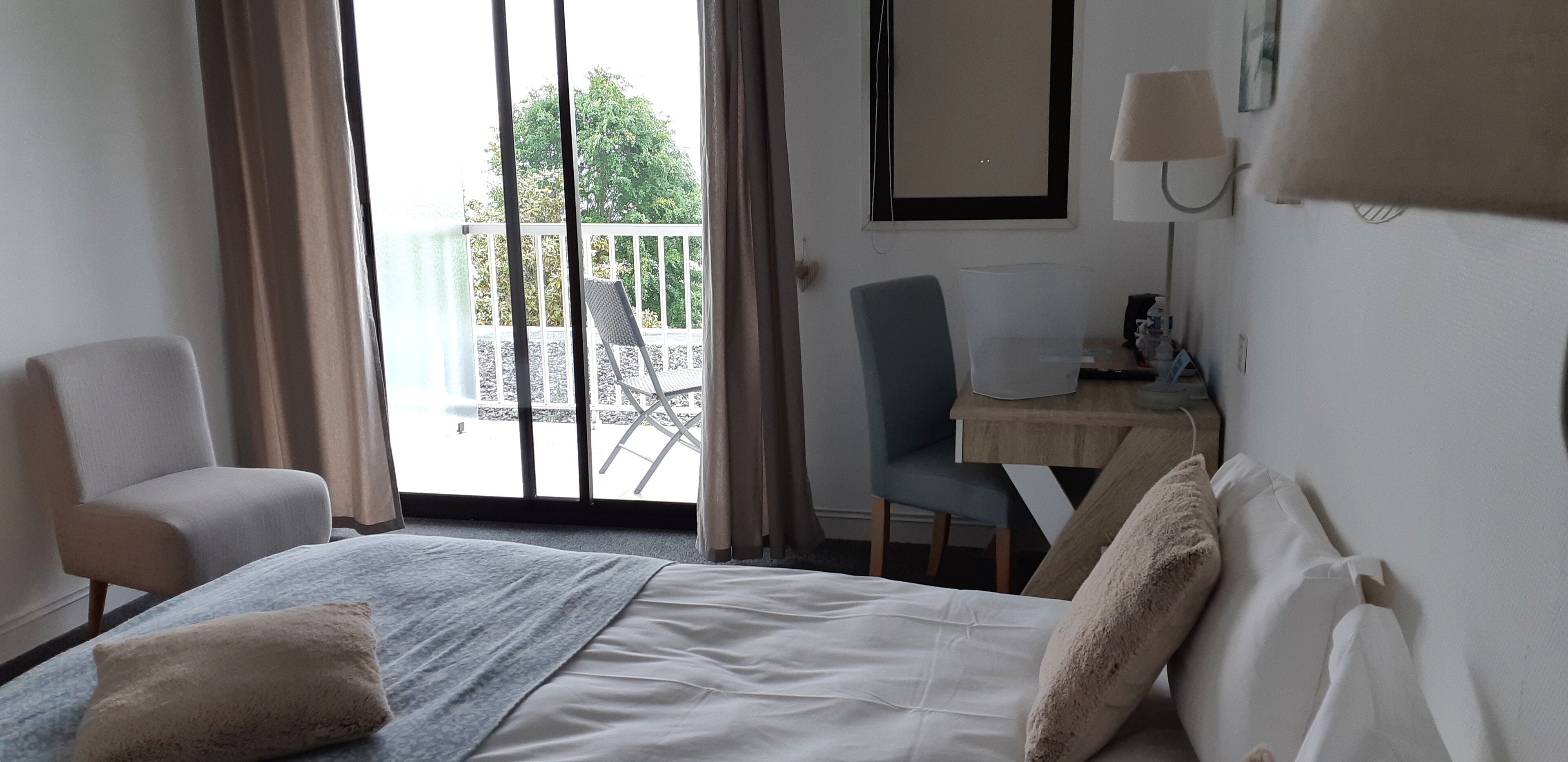 Una habitación de hotel con cama, una silla, un escritorio y un balcón con otra silla.