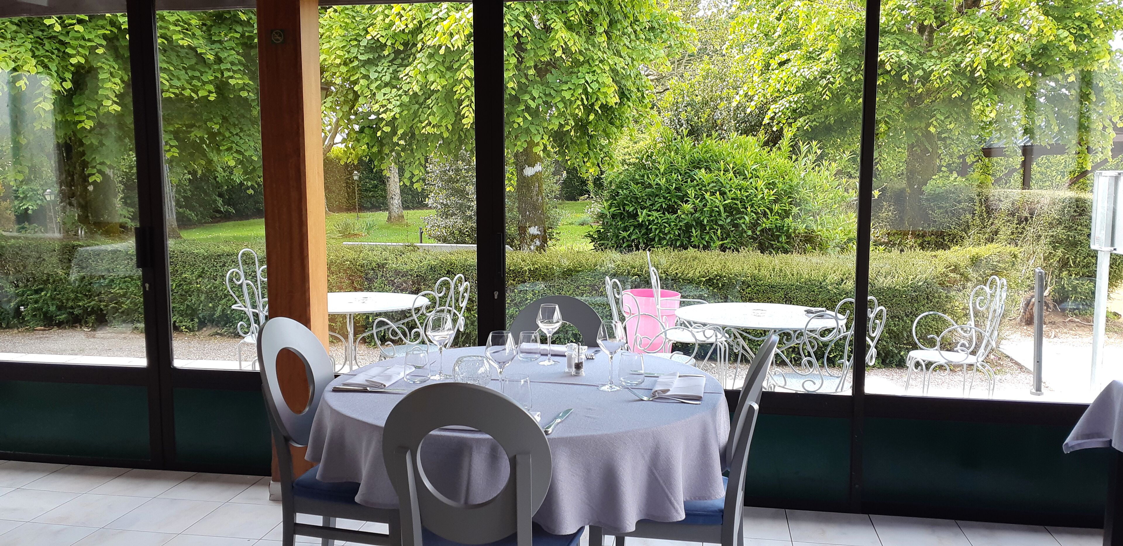 A dining area with tables set for four, surrounded by large windows offering a view of a well-maintained garden.