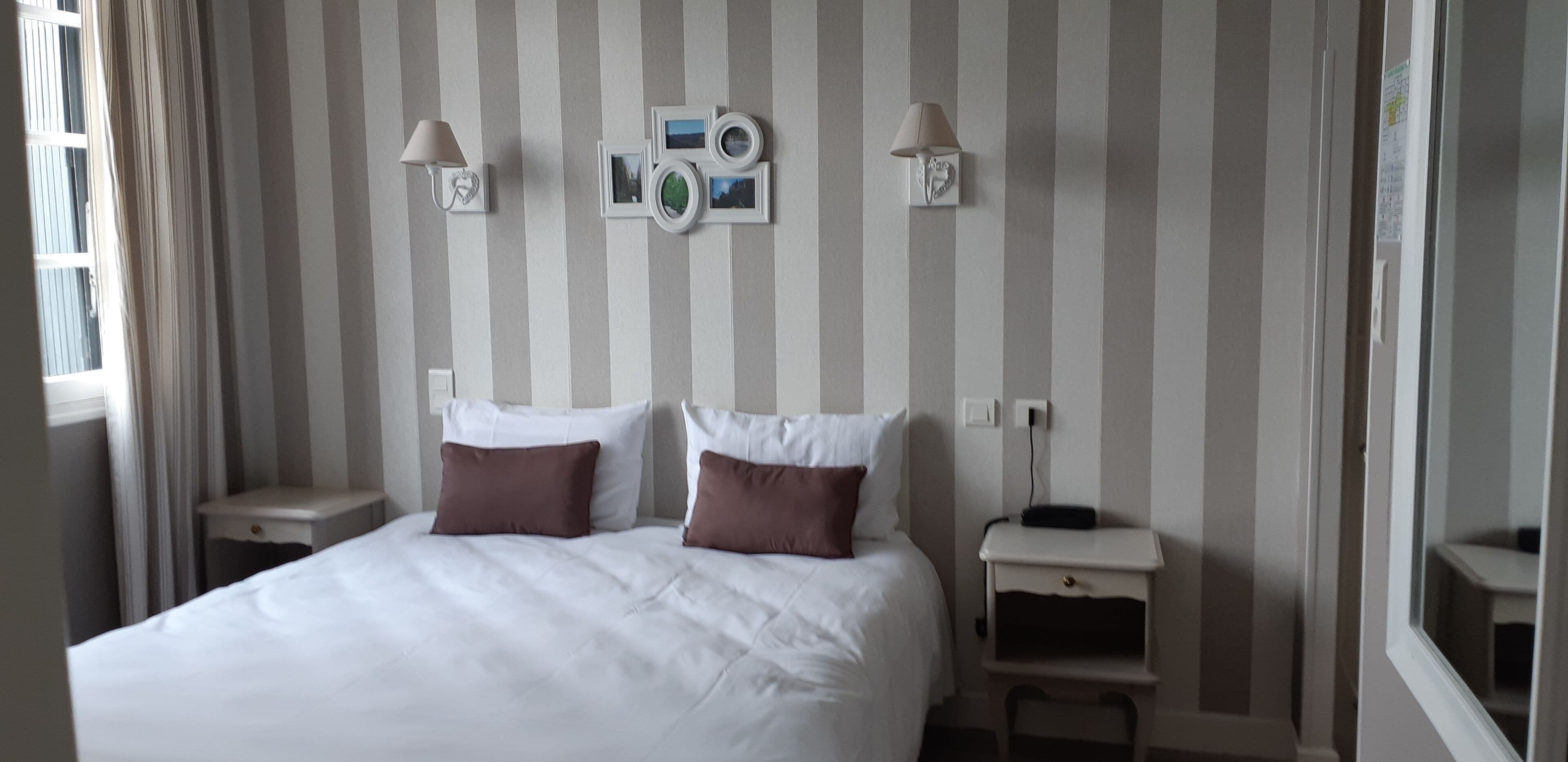A hotel room with a bed, two bedside tables, a wall-mounted lamp, and a wall decoration.