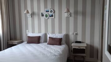 A hotel room with a bed, two bedside tables, a wall-mounted lamp, and a wall decoration.