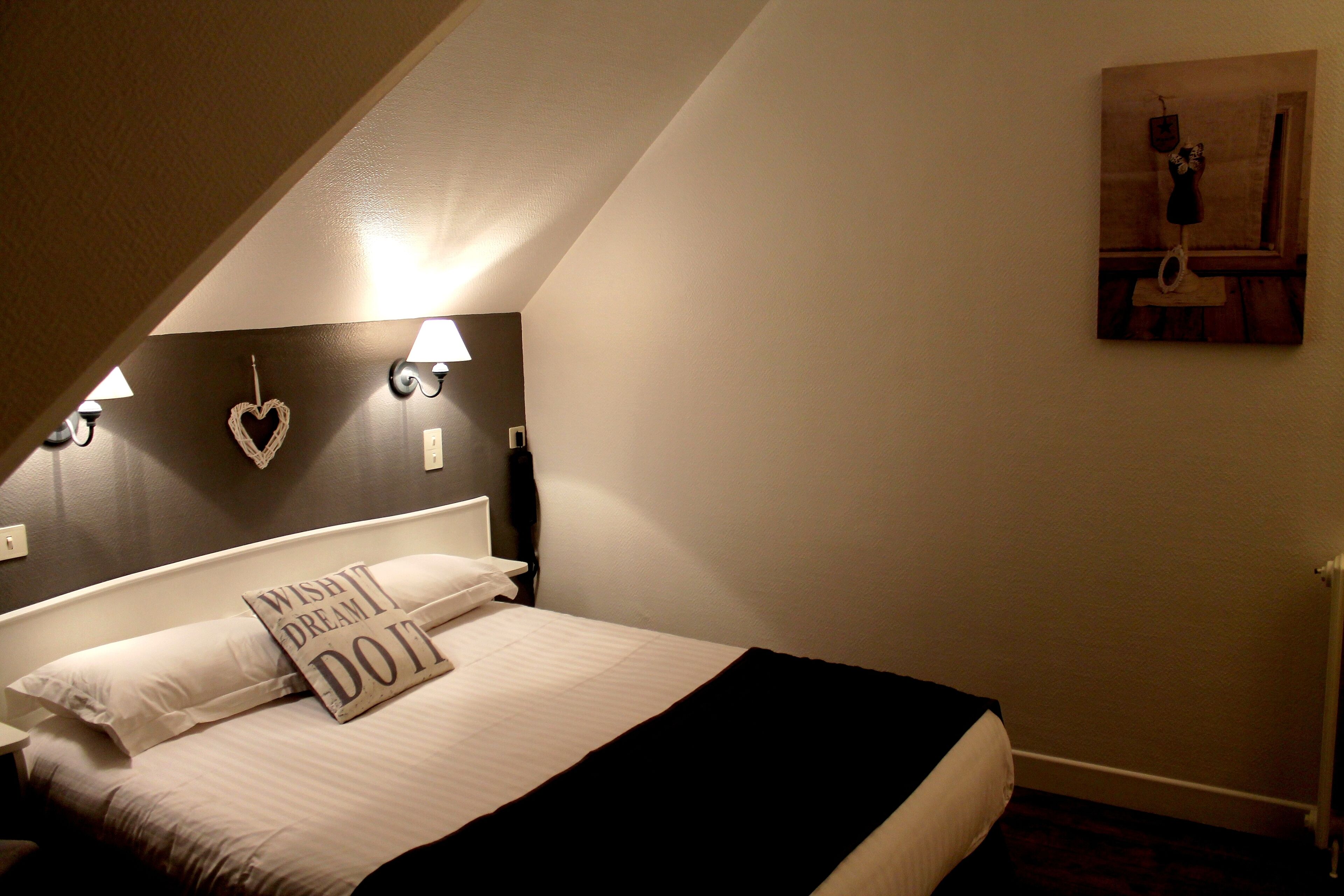 Une chambre à coucher avec un lit, une tête de lit agrémentée de lampes murales, une décoration en forme de cœur et un tableau accroché au mur.
