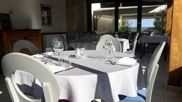 An outdoor dining area with round tables, white chairs, and a stone wall backdrop.