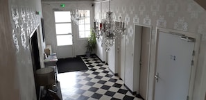 A hotel hallway with a checkered floor, a chandelier, and a door with an emergency exit sign.
