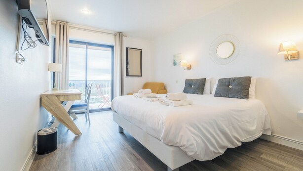 Habitación de hotel con cama, escritorio, silla, televisión y balcón con vistas.