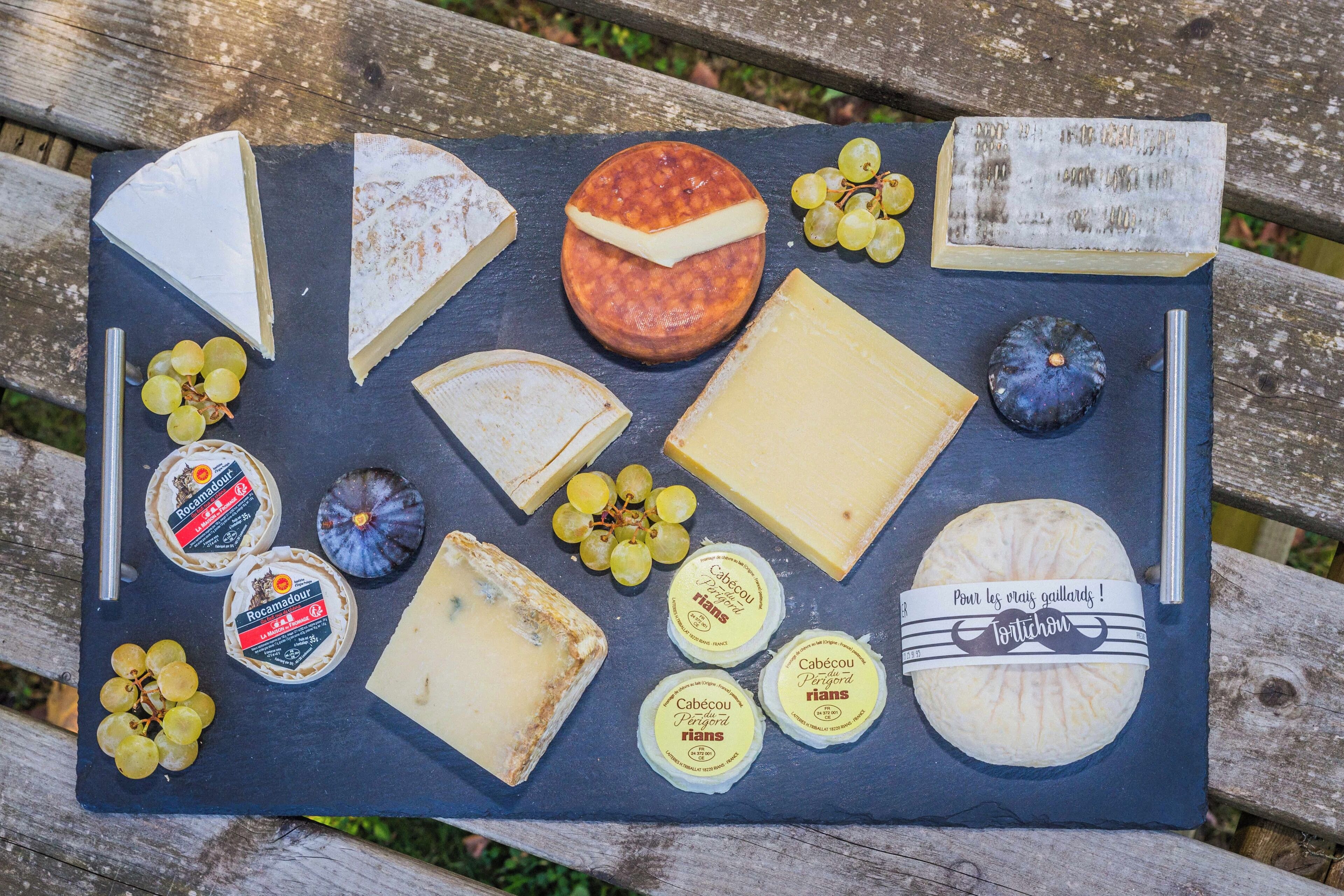 A variety of cheeses and grapes on a slate board.